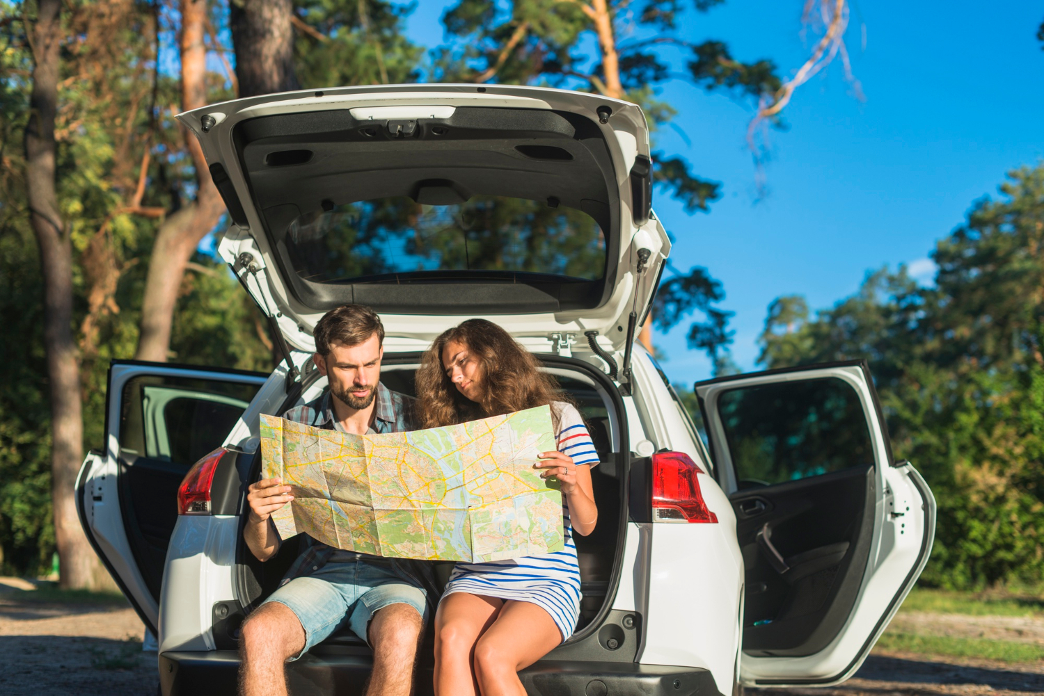 Couple sitting in the open trunk of a white car reading a map — Affordable Car Rentals Toronto Downtown.