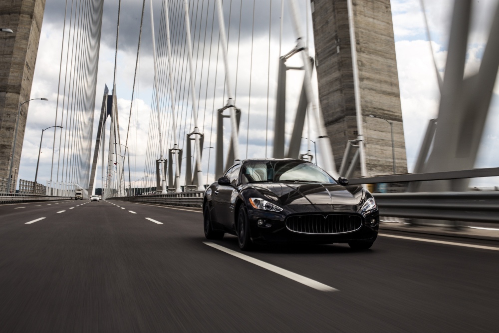 Black luxury sports car driving across a cable-stayed bridge — airport car rental.