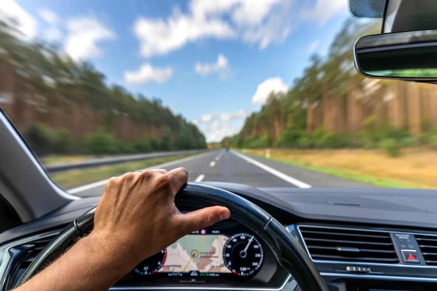 Driver perspective on open road with steering wheel and navigation screen