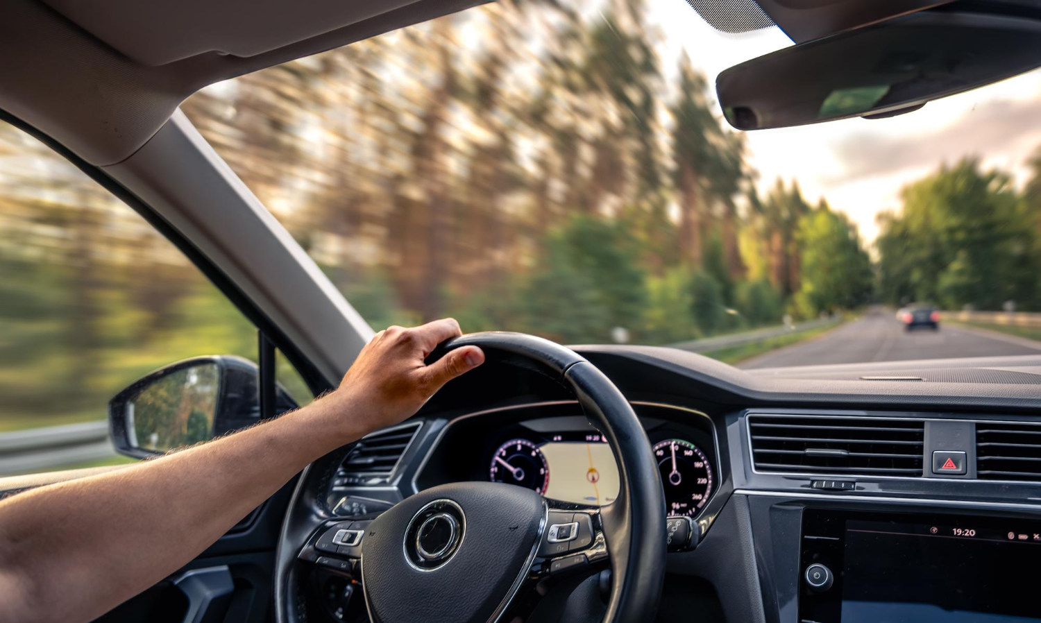 Driver's hand on steering wheel of rental car cruising past tree-lined road near Orlando.