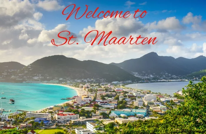 Panoramic view of St. Maarten coastline with mountains, turquoise water, and a town.