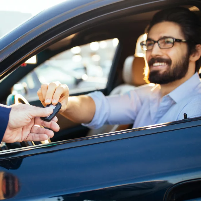 Young and handsome businessman buying car and taking keys from seller