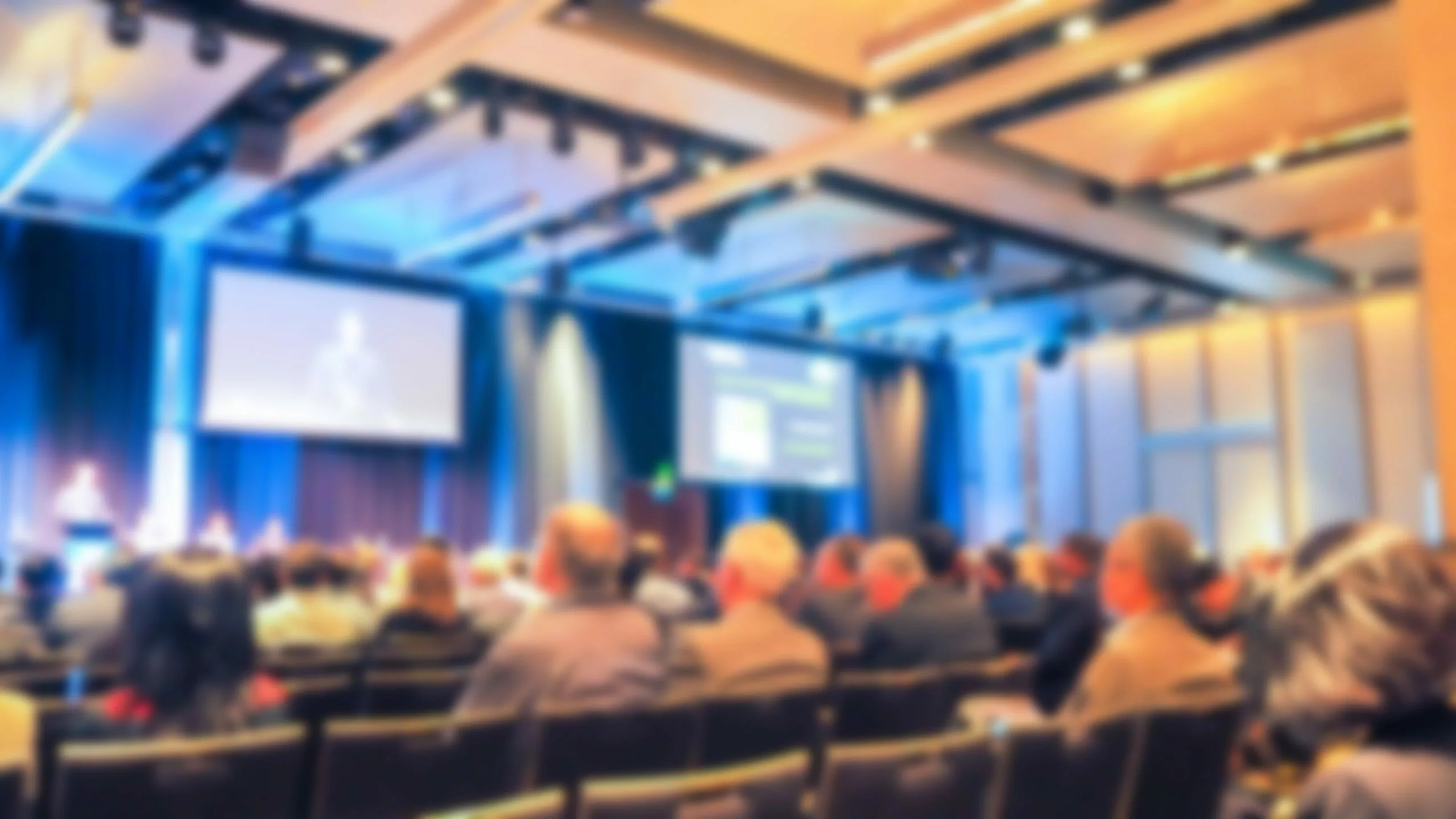 Blurry conference audience watching presenters on stage, National Geographic Live speaker — Vancouver car rentals.