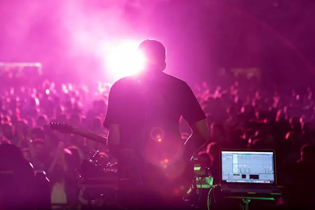 Crowd at outdoor concert with purple stage lights; audience holding up phones recording the performance.