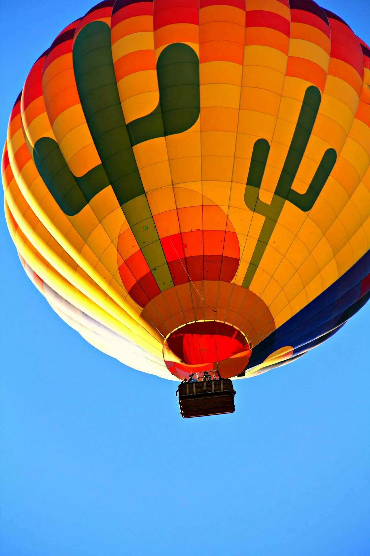 Bright yellow and orange hot air balloon filling clear blue sky, basket with passengers visible.
