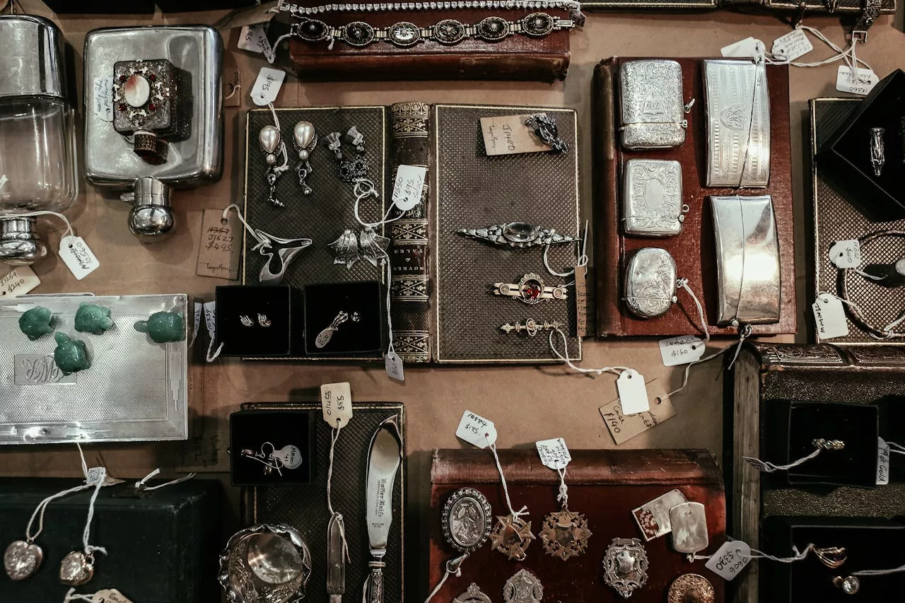 Vintage silver jewelry and small antiques displayed in boxes and trays at an antique show.