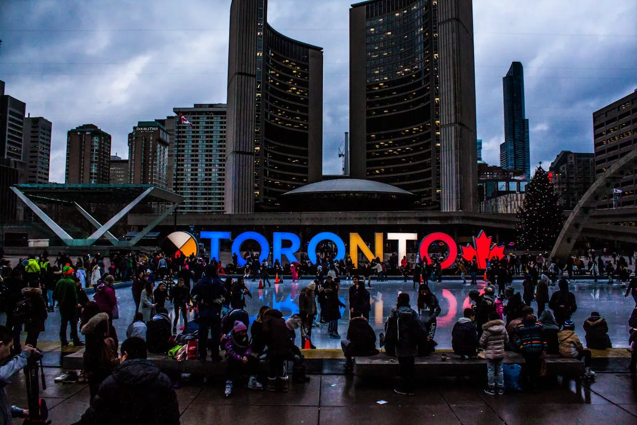 Nathan Phillips Square ice rink with "TORONTO" sign lit and crowds at a winter event.